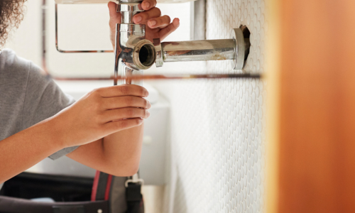 A close up of hands fixing a pipe underneath a sink