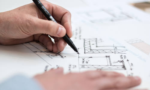 A close up of a hand holding a pen writing on a blueprint