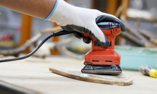 An electric hand sander being used on wood